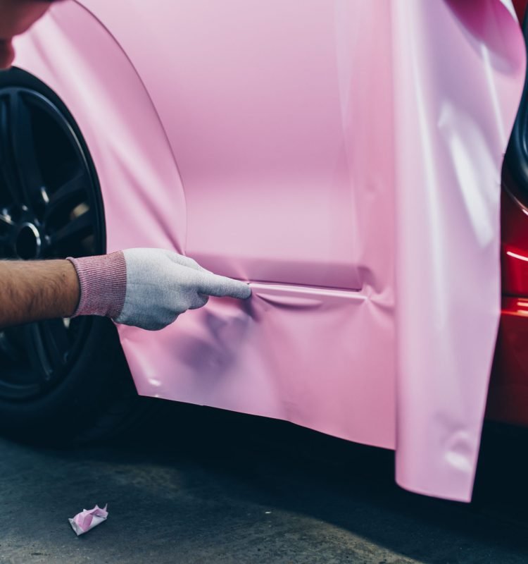 Car wrapping specialist putting vinyl foil or film on car. Selective focus.